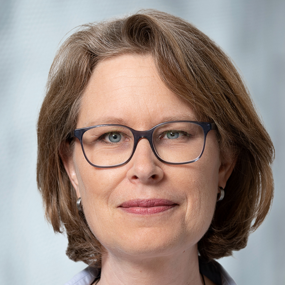 Portrait Dr. Christina Seyler, weiblich lesbare, hellhäutige Person mit mittellangen, dunkelblonden Haaren, Brille, kleinen Ohrringen, weissem Hemd